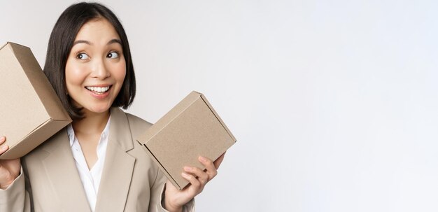 Image d'une vendeuse asiatique secouant des boîtes et devinant ce qu'il y a à l'intérieur souriant pensif debout sur fond blanc