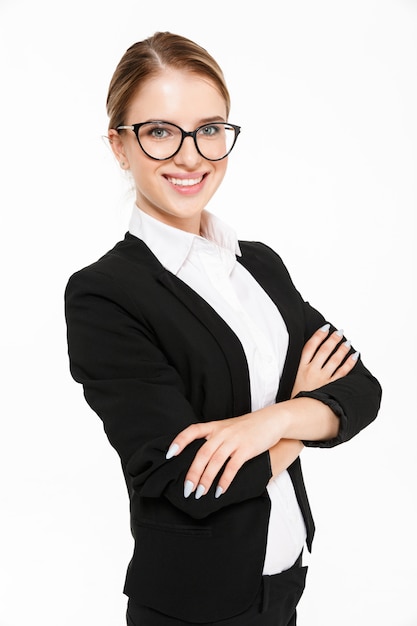 Image verticale de femme d'affaires blonde souriante à lunettes posant sur le côté avec les bras croisés sur blanc