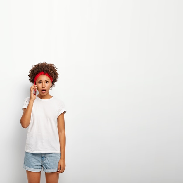 Photo gratuite image verticale d'une jeune femme stupéfaite a une conversation téléphonique avec sa sœur, découvre des nouvelles choquantes