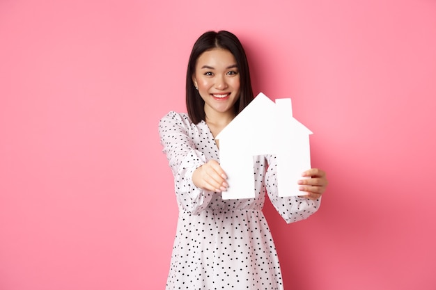 Immobilier femme asiatique adulte à la recherche d'un modèle de maison tenant une maison et promo souriante de courtier com...