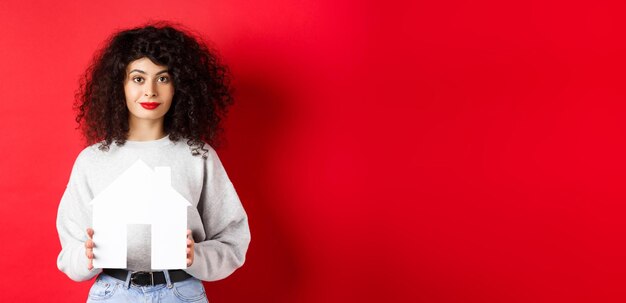 Immobilier jeune femme de race blanche dans des vêtements décontractés montrant la découpe de la maison de papier achetant une propriété ou re