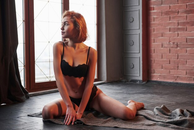 Impressionnant femme regardant. Jolie jeune fille sexy en sous-vêtements est assis sur le sol de la salle près des fenêtres
