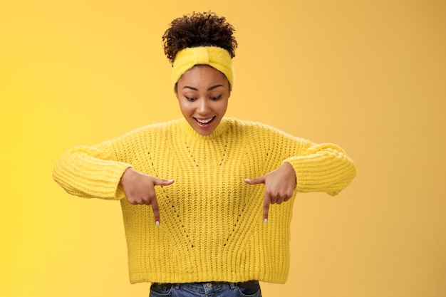 Impressionné, enthousiaste, souriant, fasciné, femme afro-américaine dans un bandeau de chandail, pointant vers le...