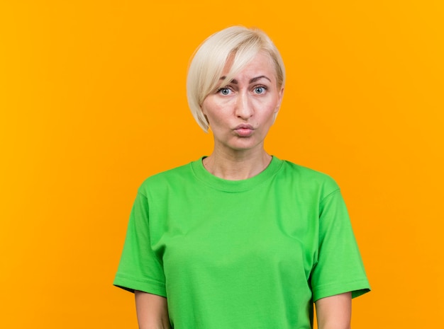 Impressionné femme blonde d'âge moyen à l'avant isolé sur mur jaune