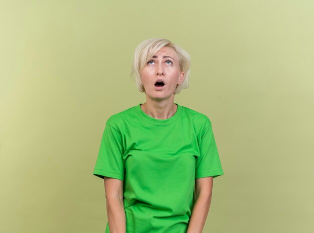 Impressionné femme blonde d'âge moyen à la recherche d'isolement sur le mur vert olive