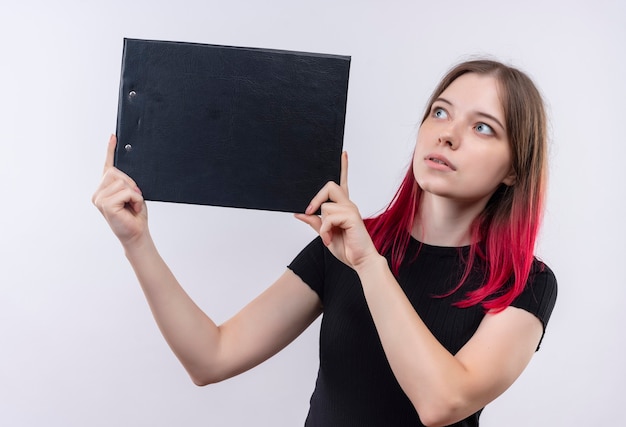 Impressionné jeune belle femme portant un t-shirt noir tenant le presse-papiers sur un mur blanc isolé