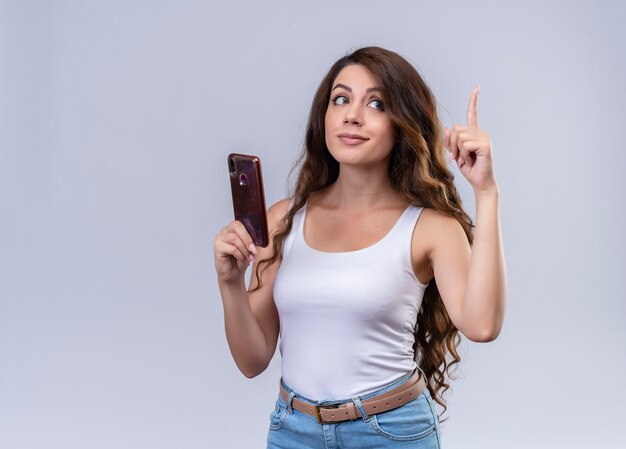 Impressionné jeune belle fille tenant un téléphone mobile en levant le doigt avec espace de copie