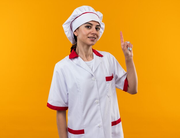 Impressionné jeune belle fille en uniforme de chef pointe vers le haut