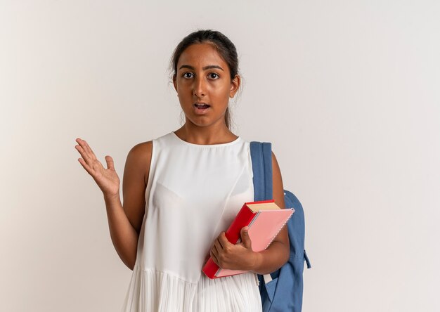 Impressionné jeune écolière portant sac à dos tenant livre avec ordinateur portable et montrant avec la main à côté