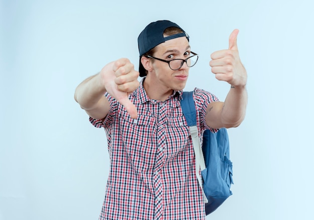 impressionné jeune étudiant garçon portant un sac à dos et des lunettes et bonnet ses pouces de haut en bas