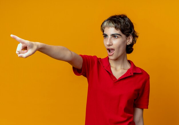 Impressionné jeune femme avec coupe de cheveux de lutin à la recherche et pointant sur le côté