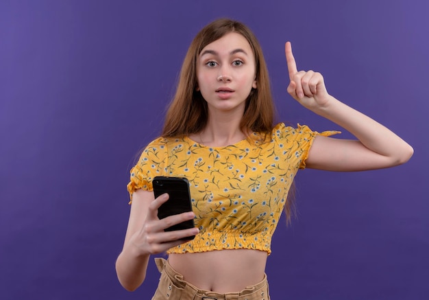 Impressionné jeune fille ayant une nouvelle idée, tenant un téléphone mobile et levant le doigt sur un espace violet isolé avec espace copie