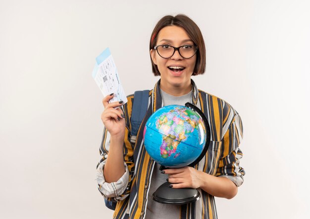 Impressionné jeune fille étudiante portant des lunettes et sac à dos tenant des billets d'avion et globe isolé sur blanc