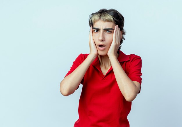 Impressionné jeune fille de race blanche avec coupe de cheveux de lutin mettant les mains sur le visage isolé sur fond blanc avec espace de copie