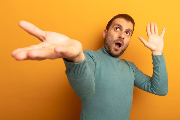 Impressionné jeune homme de race blanche qui s'étend la main montrant la main vide à la recherche d'isolement sur le mur orange