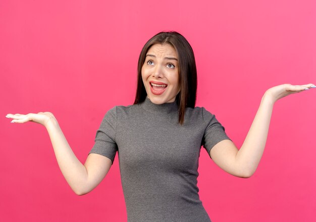 Impressionné jeune jolie femme regardant et montrant les mains vides isolés sur fond rose