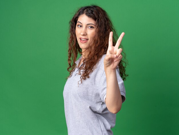 Impressionné jeune jolie fille caucasienne debout dans la vue de profil faisant signe de paix isolé sur mur vert avec espace de copie