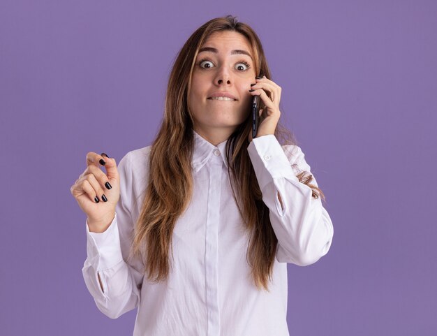 Impressionné jeune jolie fille caucasienne parle au téléphone isolé sur mur violet avec espace copie