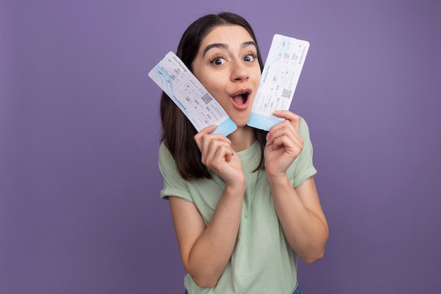 Impressionné jeune jolie fille caucasienne tenant des billets d'avion touchant le visage avec eux