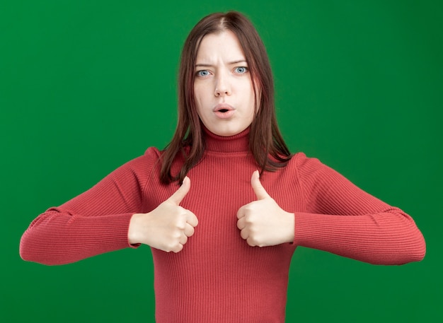 Impressionné jeune jolie fille montrant les pouces vers le haut isolé sur mur vert