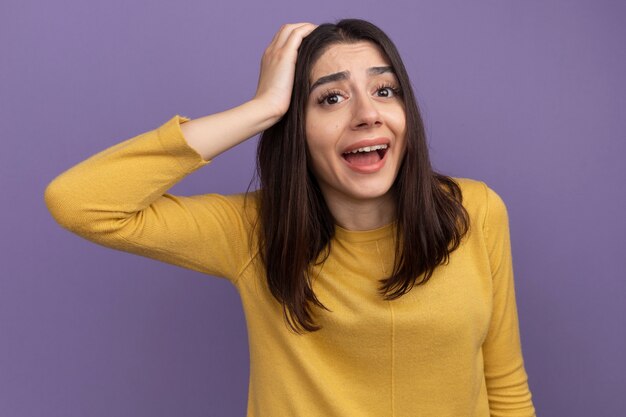 Impressionné jeune jolie fille de race blanche gardant la main sur la tête en regardant droit