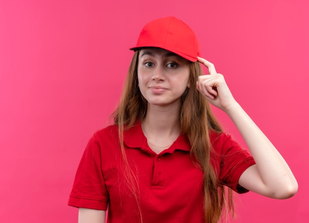 Impressionné jeune livreuse en uniforme rouge mettant le doigt sur la tête sur l'espace rose isolé avec copie espace