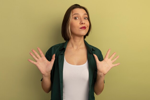 Impressionné jolie femme se tient avec les mains surélevées isolé sur mur vert olive