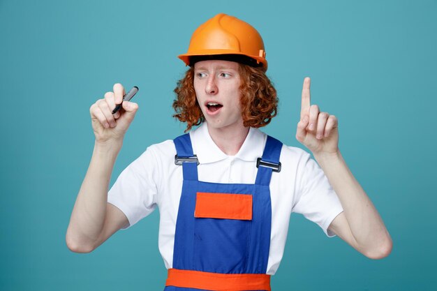 Impressionné montrant le nombre de jeunes constructeurs en uniforme tenant un marqueur à la caméra isolé sur fond bleu