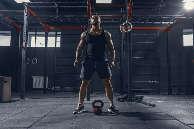 Inarrêtable. Jeune athlète caucasien musclé pratiquant des squats dans une salle de sport avec le poids. Modèle masculin faisant des exercices de force, formation du bas du corps. Bien-être, mode de vie sain, concept de musculation.