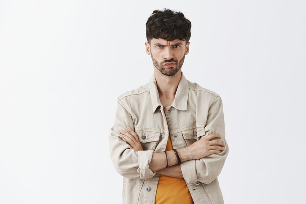 Incertain barbu élégant à l'air sérieux posant contre le mur blanc