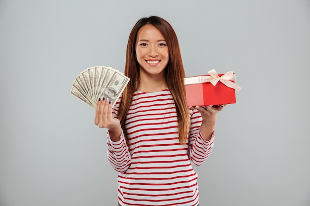 Incroyable émotionnelle jeune femme asiatique tenant cadeau et argent.