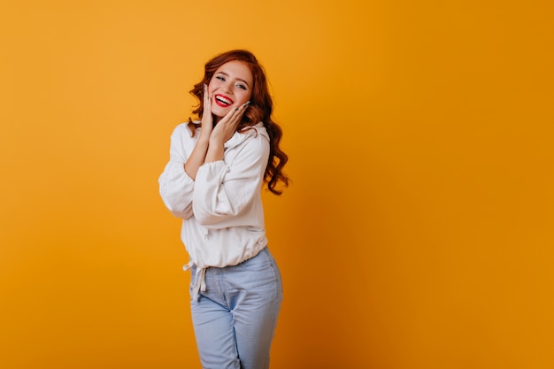 Incroyable femme aux cheveux longs souriant sur le mur jaune. Superbe modèle féminin au gingembre posant en pull blanc.