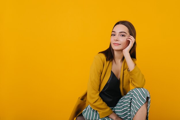 Incroyable femme européenne touchant son visage. Portrait intérieur d'une femme spectaculaire aux yeux bruns.