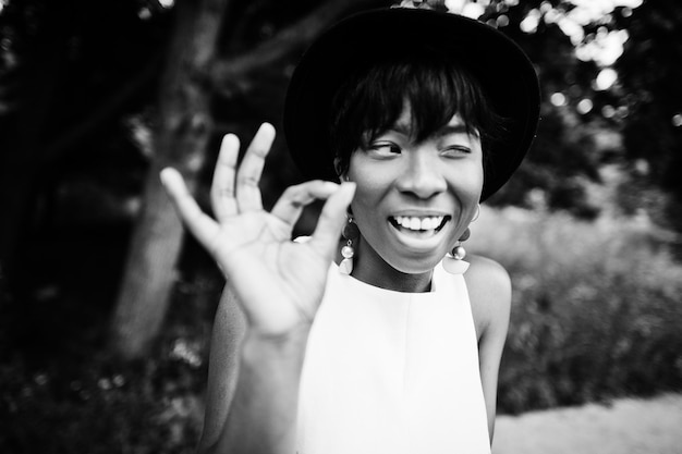 Photo gratuite incroyable femme modèle afro-américaine en pantalon vert et chapeau noir posé au parc montre des doigts ok