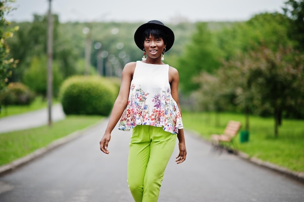 Incroyable femme modèle afro-américaine en pantalon vert et chapeau noir posé avec différentes émotions au parc