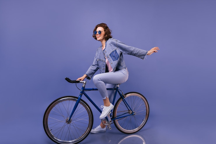 Photo gratuit incroyable femme en vêtements de printemps assis à vélo. portrait intérieur de jolie fille à lunettes de soleil s'amuser.