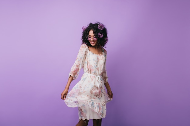 Incroyable fille brune posant en robe d'été à la mode. Portrait d'une femme africaine magnifique dansant avec un sourire inspiré.