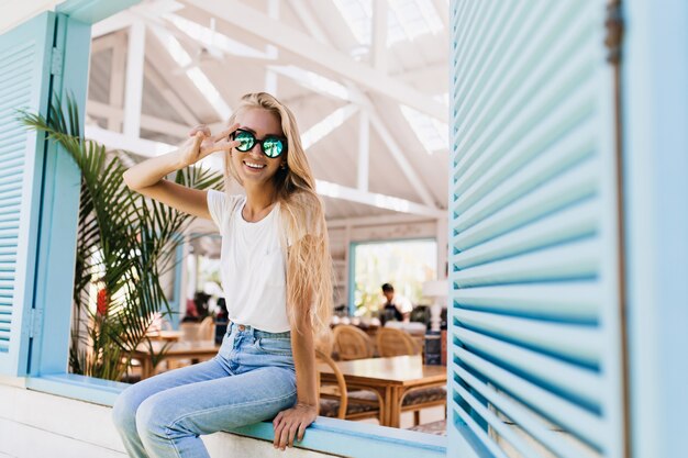 Incroyable modèle féminin européen en t-shirt blanc posant dans des lunettes de soleil éclatantes et un jean bleu.