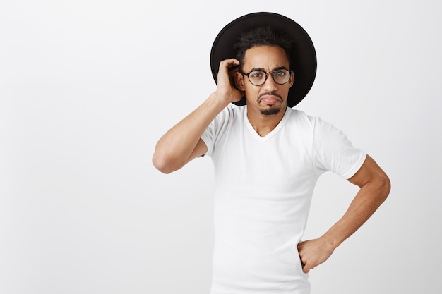 Photo gratuite indécis bel homme afro-américain à lunettes et tête de grattage de chapeau perplexe, à la confusion