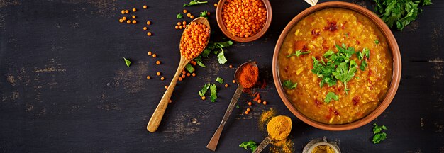 Indian Dhal curry épicé dans un bol, épices, herbes, table en bois noir rustique.