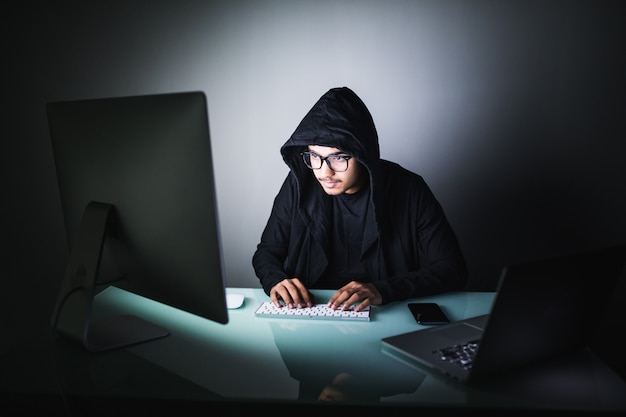 Photo gratuite indian hacker dans un sweat à capuche sombre assis devant un ordinateur portable. attaque de confidentialité informatique