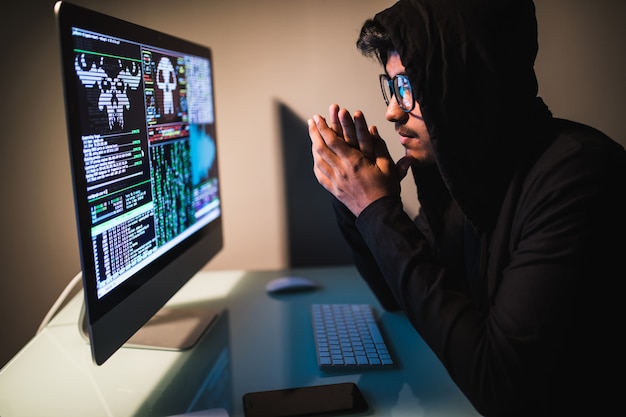Indianmale hacker avec smartphone et codage sur écran d'ordinateur dans une pièce sombre
