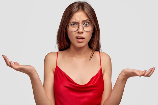 indigné jeune femme brune posant contre le mur blanc