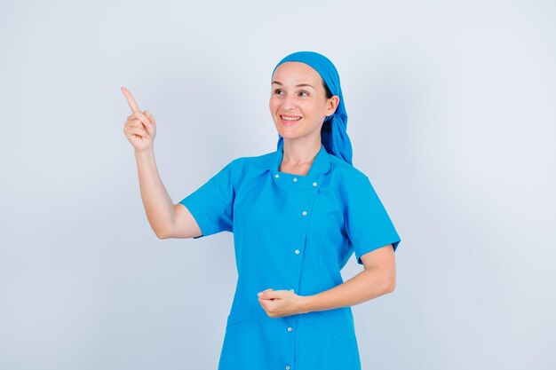 Une infirmière heureuse regarde et pointe vers le haut avec l'index sur fond blanc