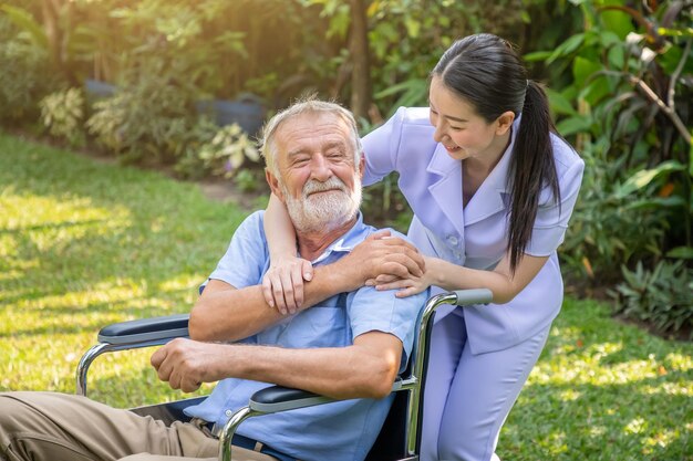 Infirmière heureuse tenant la main d'un homme âgé sur un fauteuil roulant dans le jardin d'une maison de retraite