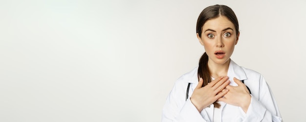 Photo gratuite infirmière médecin choquée à la recherche d'inquiétude et surprise à l'appareil photo tenant la main sur le cœur debout dans wh