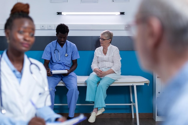 Photo gratuite infirmière médicale examinant le dossier du rapport du patient assis sur un lit d'hôpital avec une femme âgée malade. personnel médical analysant les résultats de la consultation et la documentation du patient pour un rendez-vous