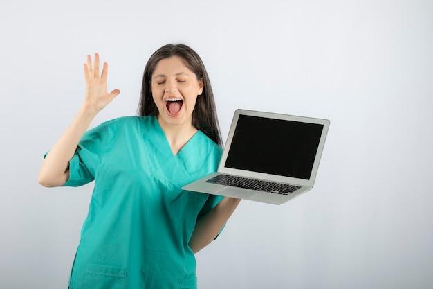 Infirmière positive posant avec ordinateur portable sur blanc.