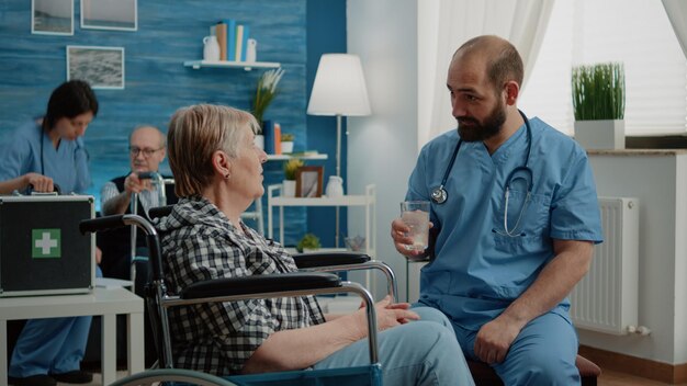 Infirmière préparant une pilule effervescente dans un verre d'eau pour un patient en maison de retraite. Assistant médical donnant une boisson vitaminée à une vieille femme handicapée en fauteuil roulant pour des soins de santé.