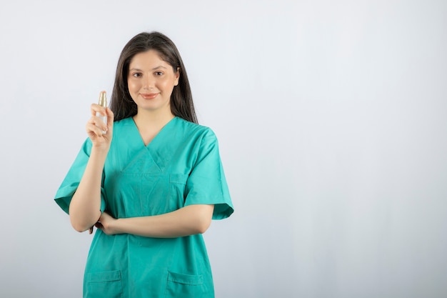 Infirmière souriante montrant un vaporisateur sur blanc.